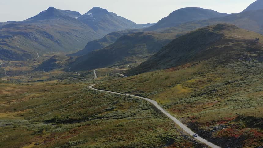 A vehicle drives down a curvy road toward rolling hills