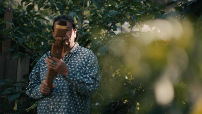 A native american man examines a traditional instrument before looking into the camera