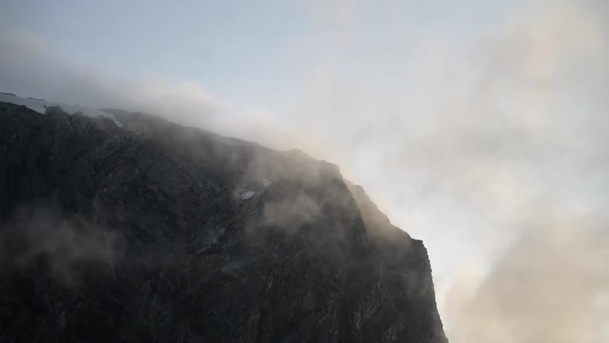 Fog floats across sky obscuring snow dabbed mountain slope