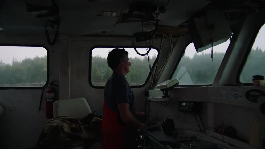 A man is standing as he steers a boat on the water