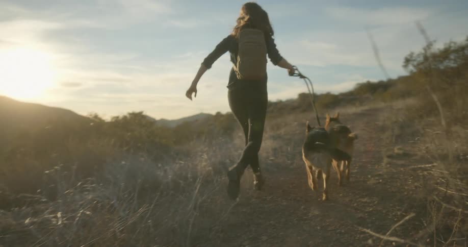 A woman is jogging outdoors with her dogs