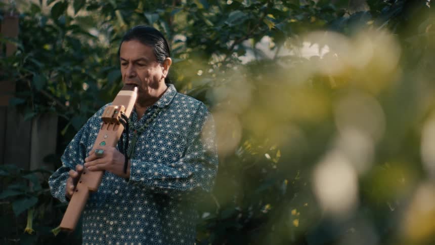 A man is standing in a group of trees and playing a musical instrument