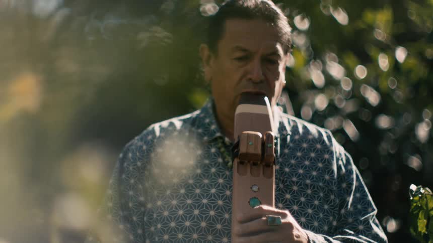 A native american man blows into a traditional woodwind instrument