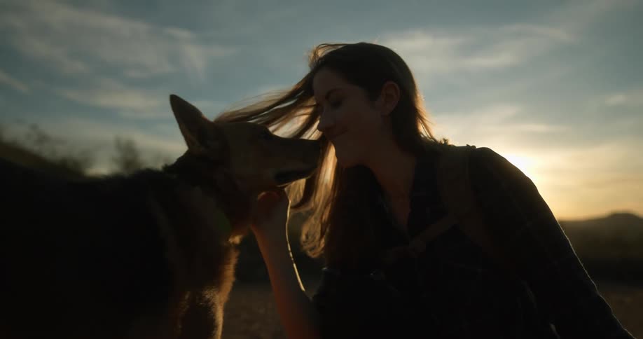 A woman is sitting outdoors with her dog while the sun sets