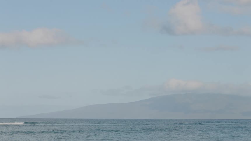 Waves are rolling across the water with a mountain in the distance and a few clouds in the sky