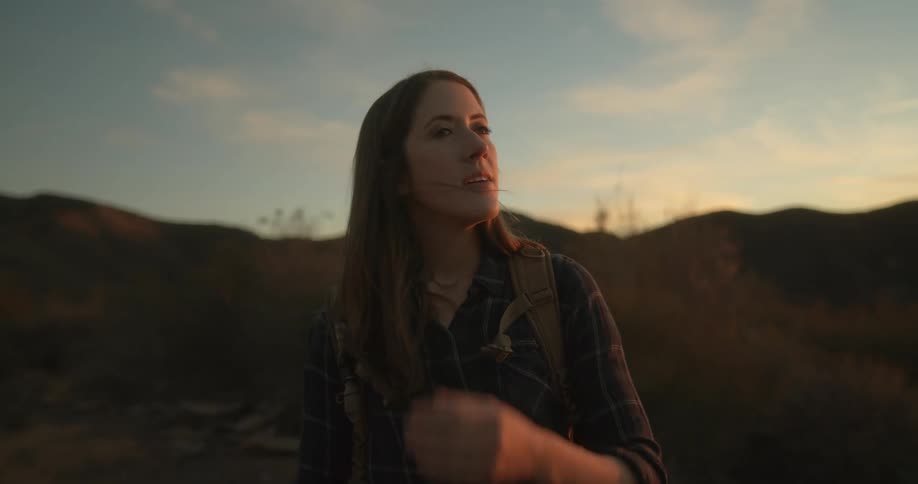 A woman is happily standing outdoors at dusk