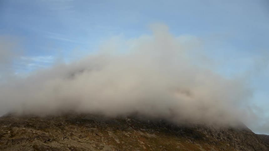 Clouds thicken and pass over a mountain covering the peak