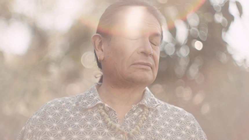 A native american looks around at his surroundings before turning to look into the camera while standing outdoors during the day