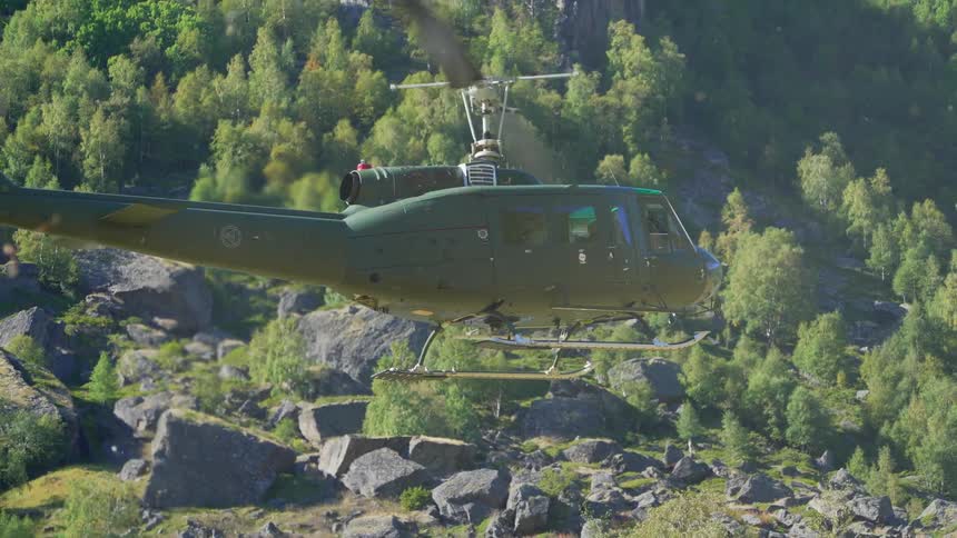 A green helicopters rotor is turning and it is lifting off the ground