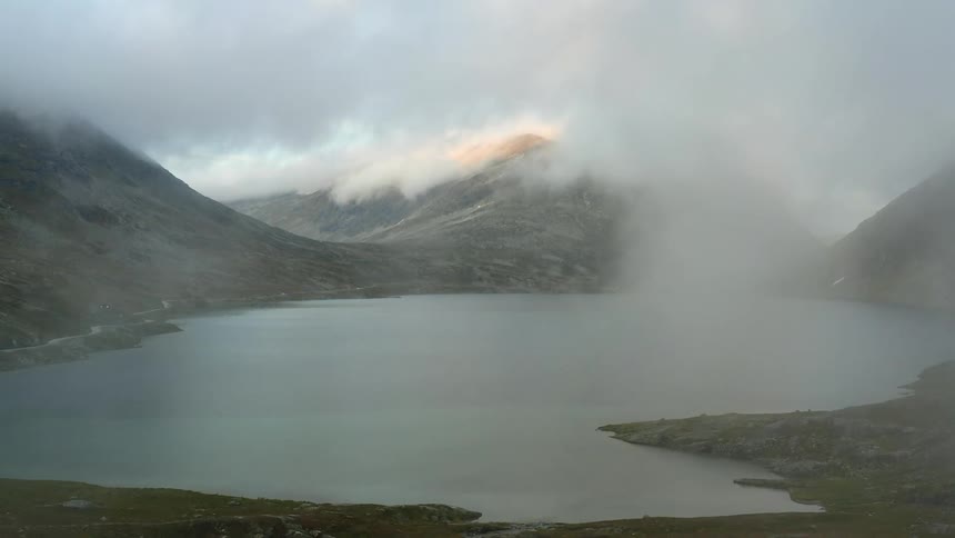 A lake shrouded in fog at the base of a mountain during the day