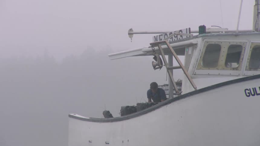 A man is moving equipment around on a boat in heavy fog