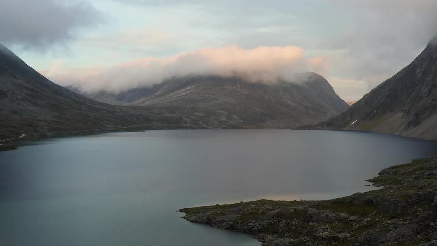 Rough algae covered terrain leads to lake and cloud topped mountain