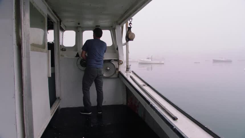 Captain driving a fishing boat on a lake through the fog at day