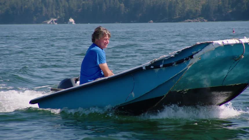 Man driving a small motor boat on a calm lake near the pine tree forest