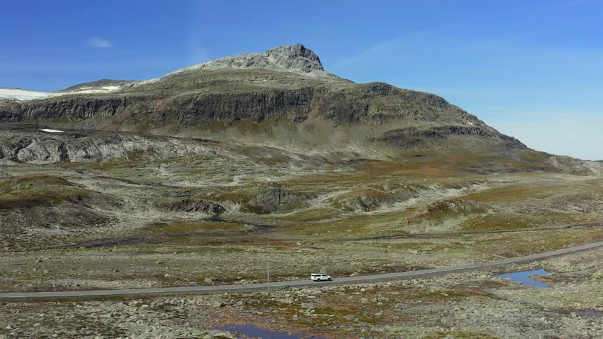 Aerial view of a white vehicle driving on a road near a mountain peak at daytime