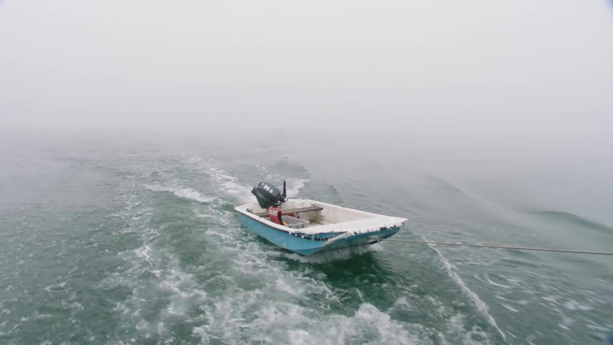 A small motor boat with a tackle box inside is being pulled across the water by a cable
