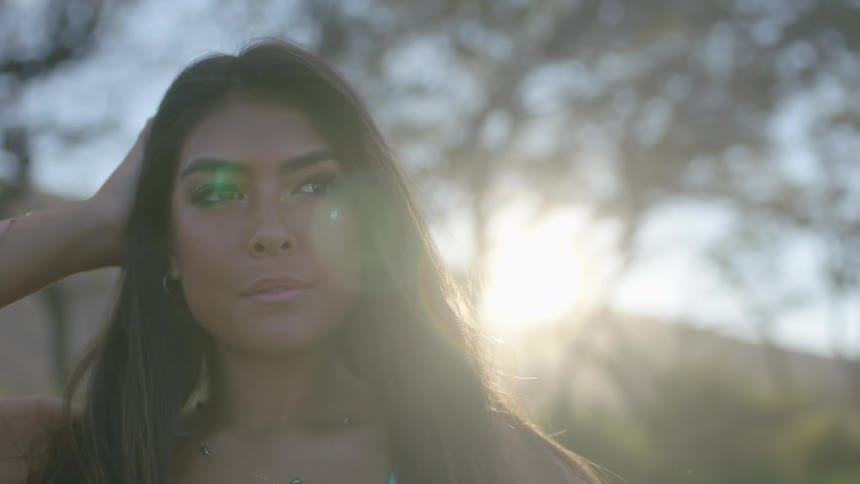 Sunlight filters through the tree branches behind a young attractive woman