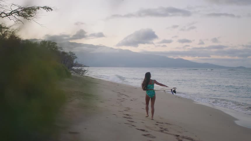 A woman walking with a surfboard down the beach