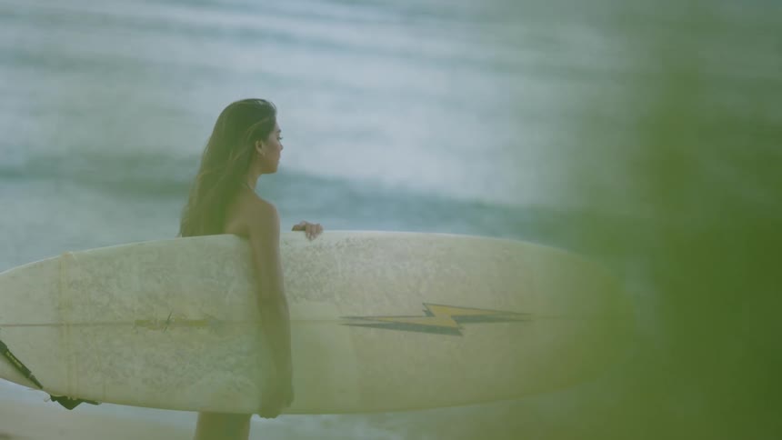 Woman on the beach holding a surfboard looking around