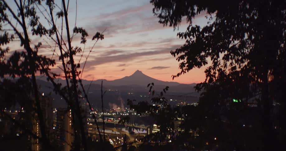View of industrial city with distant volcano under red sky