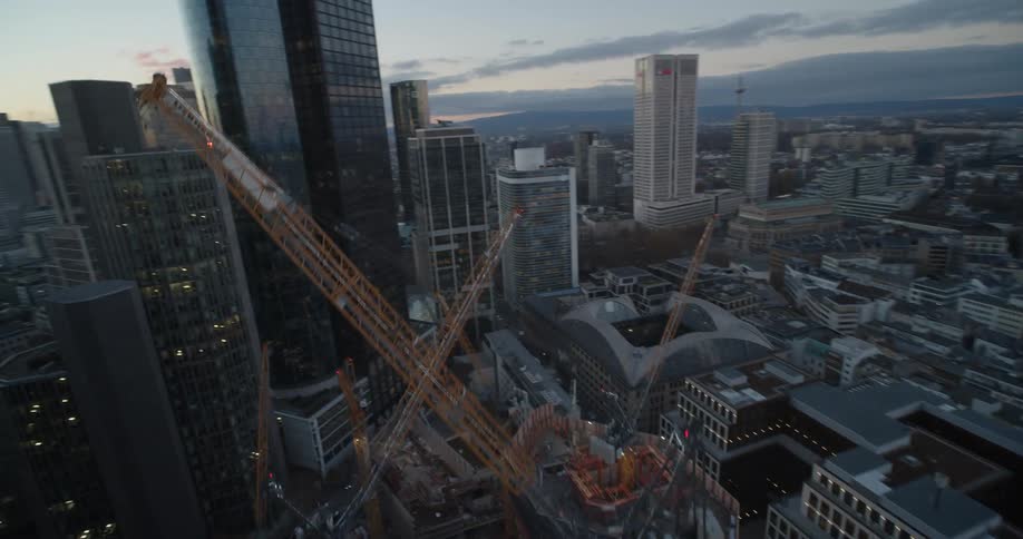 Construction cranes sit at construction site in downtown tower block with red sky on horizon