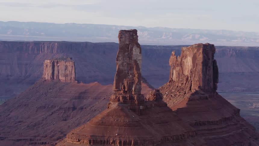 The sun shines on tall rock formations and there are mountains in the distance