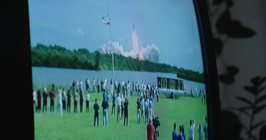 A television in a home plays with a large group watching a rocket launch on the screen