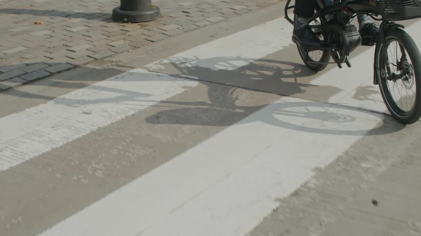 A bike riders shadow is cast on the brick sidewalk and pavement as they ride on a sunny day