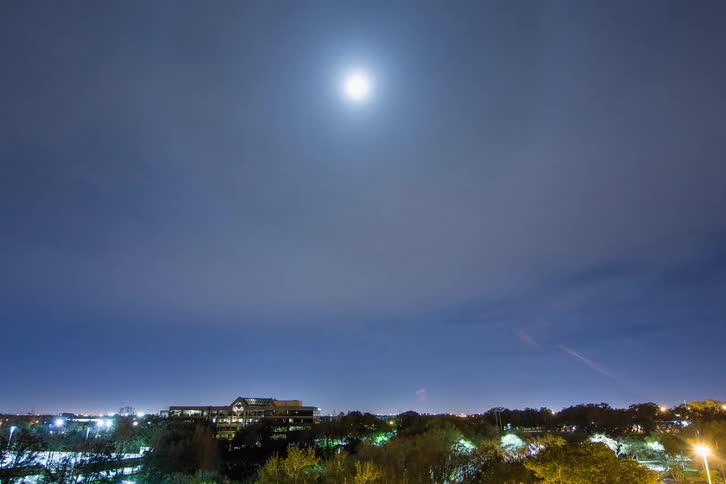 A bright meteor falls from the night sky into a neighborhood as the clouds are rapidly moving overhead