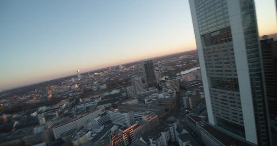 Sun shines from horizon through skyscrapers near construction site with river in the distance