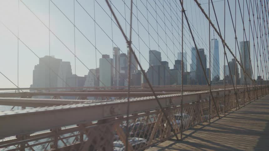 Man rides a bicycle over the brooklyn bridge close to the city skyline at sunset