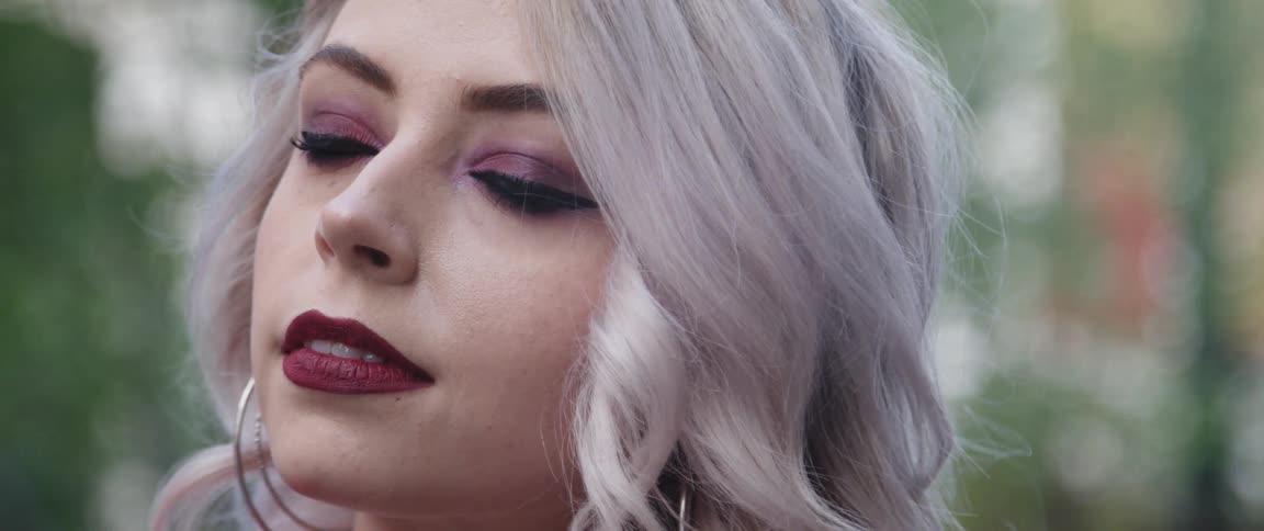 Woman with makeup gray hair and hoop earrings looks at camera