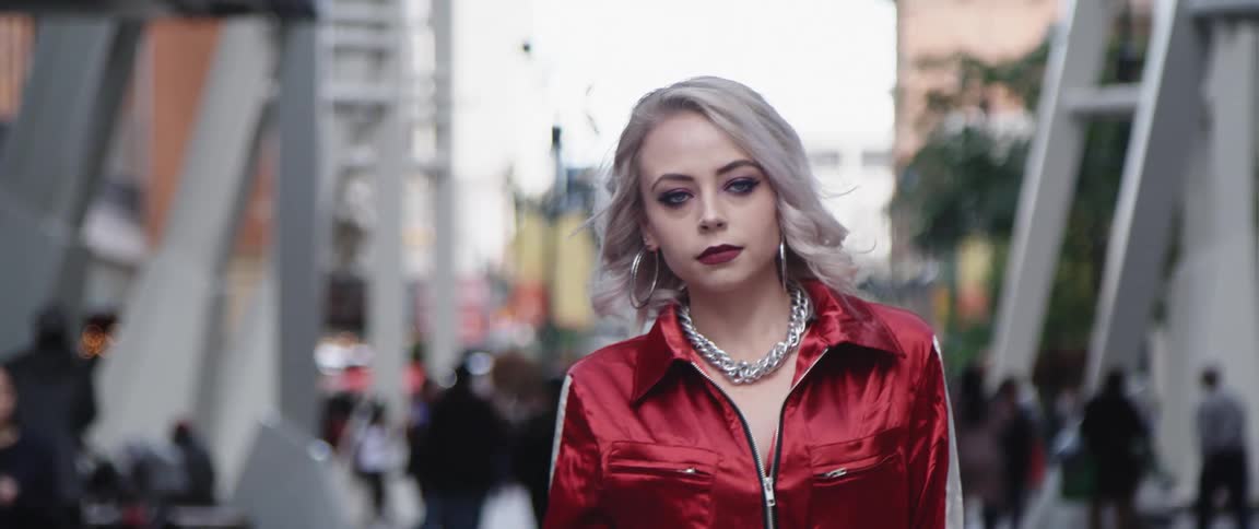 Woman with makeup gray hair hoop earrings and red jacket walks down the city street