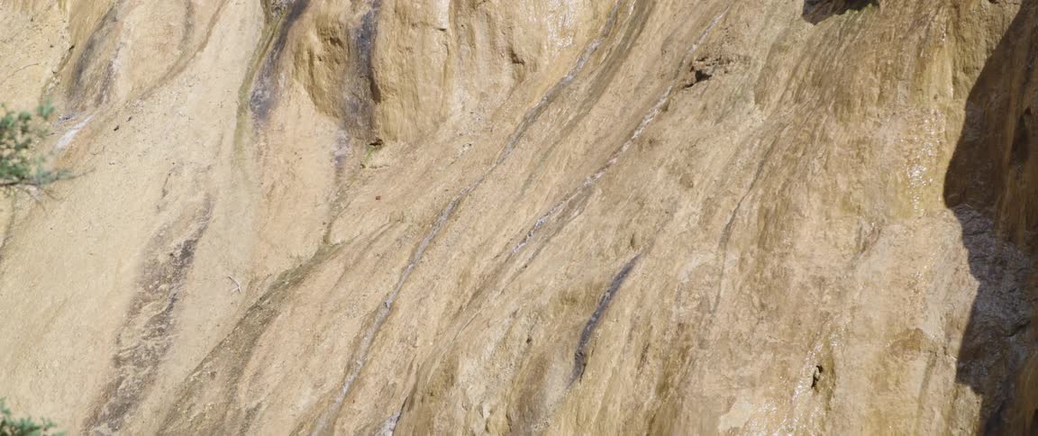 Streams of water run down a sheer rock cliff during the day
