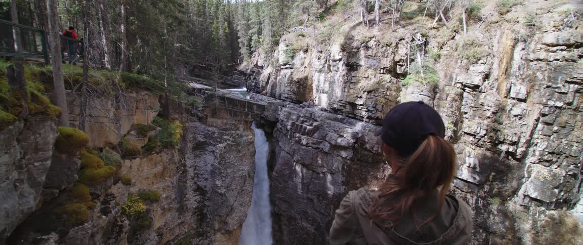 Woman standing on an observation deck looks at a waterfall in the mountains