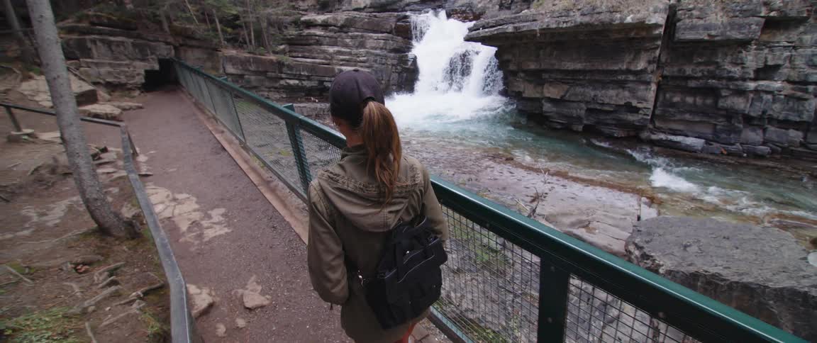 A woman is hiking past a waterfall and stream