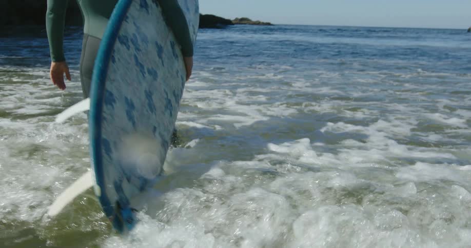 Woman wearing a wet suit holds a surfboard while standing on the ocean at morning
