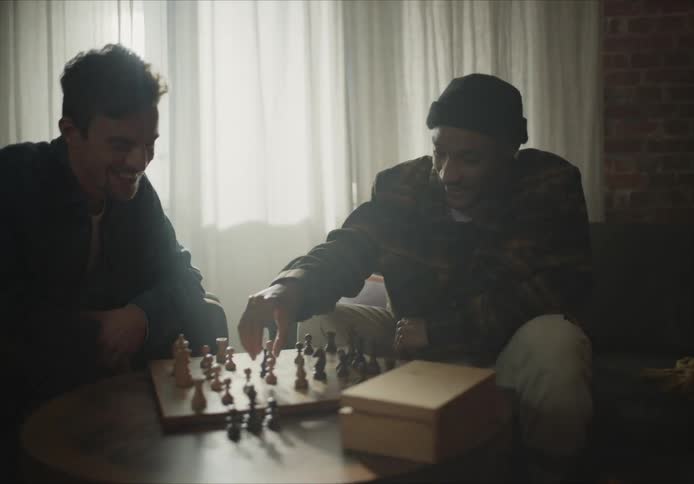 Two men laugh as they play a game of chess at home