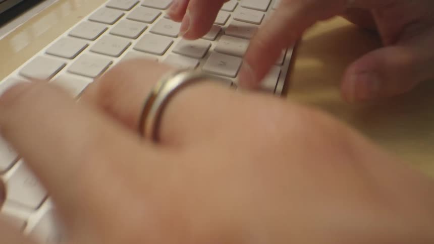 Man with tattoed arms sitting at a desk typing on a white computer keyboard