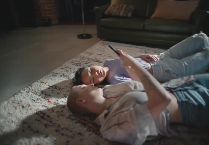 Two women lay on the floor together looking at a cell phone and laughing