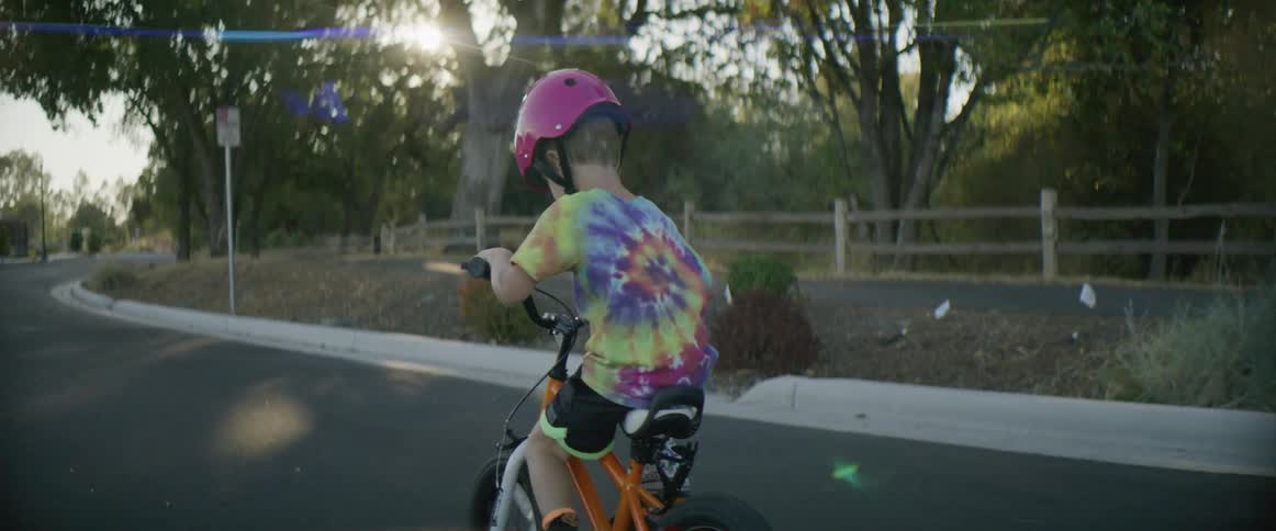 Child wearing crash helmet pedals along street through neighborhood before looking to the side and smiling