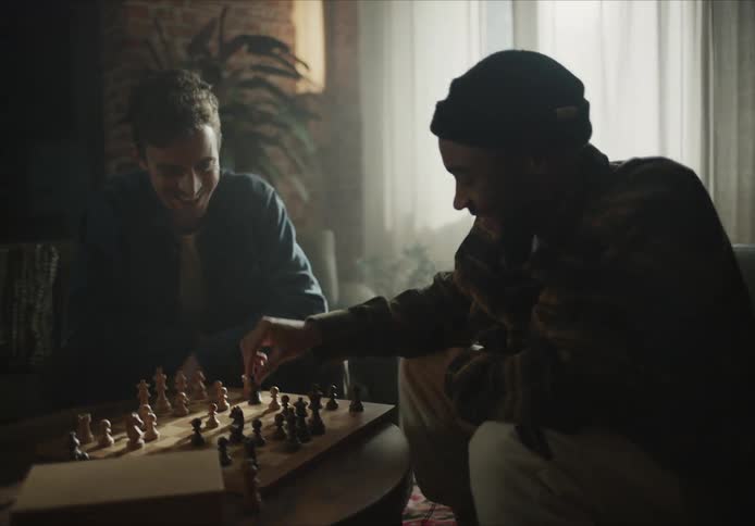 Two men sitting in armchairs play chess talking and laughing in living room at home