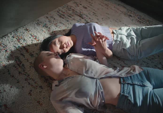 Two women lay on the floor together holding hands