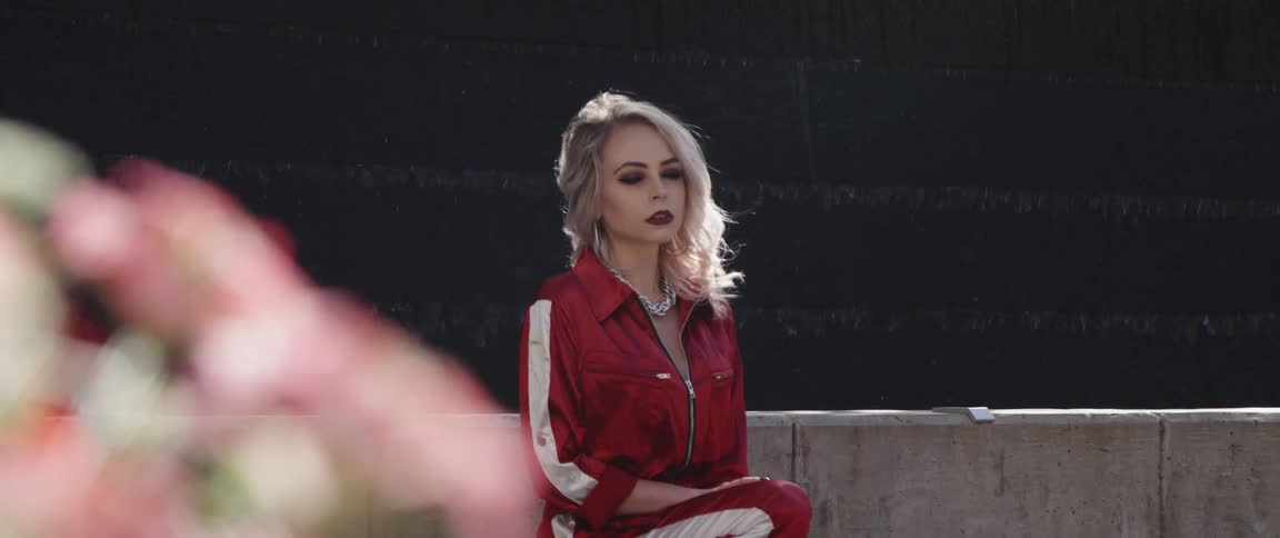 Blonde woman wearing red tracksuit modeling for the camera in front of a fountain