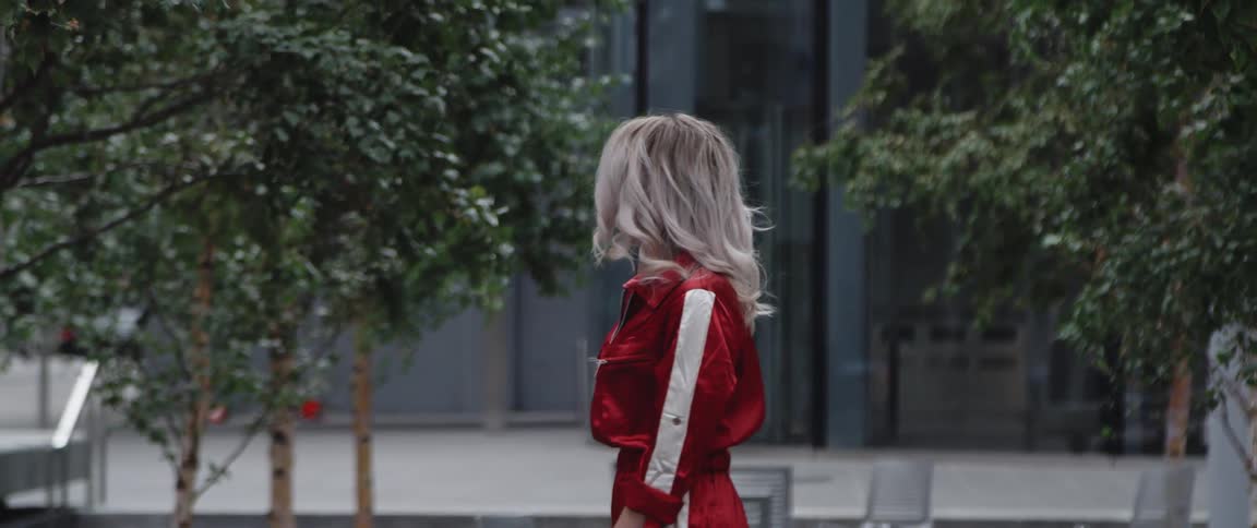 A woman standing outdoors in a city turns around to look into the camera