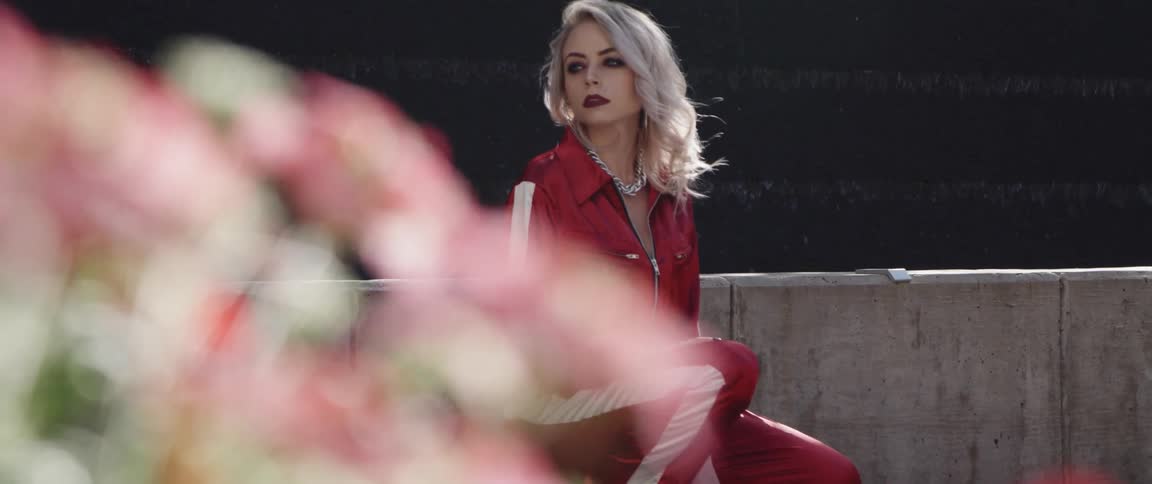 A woman wearing a red jumpsuit poses outside near a wall