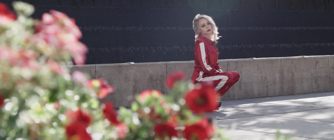 Woman wearing a red track suit crouching in front of a fountain behind flowers