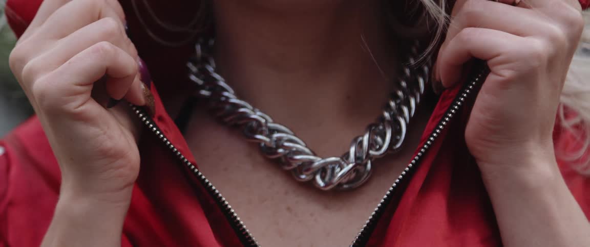 Woman pulls collar open to allow clear view of large chained silver necklace
