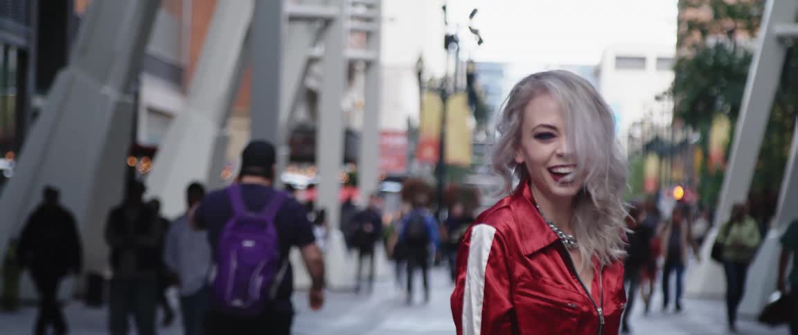 A woman smiles wide as she poses on a busy city sidewalk