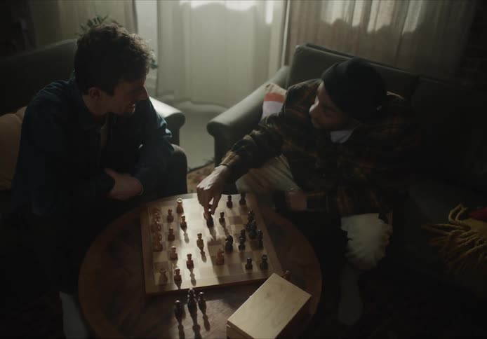 Two men sit in chairs playing chess together and laughing